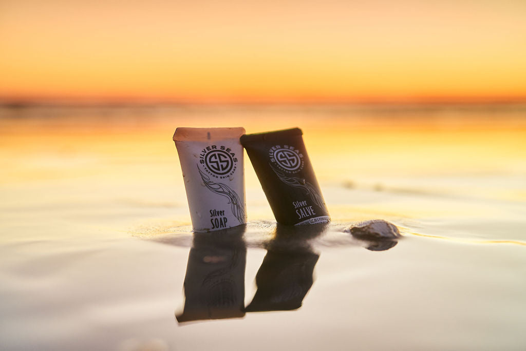 Two tubes Silver Seas Skin Care products Microsilver BG™ partially covered with beach sand